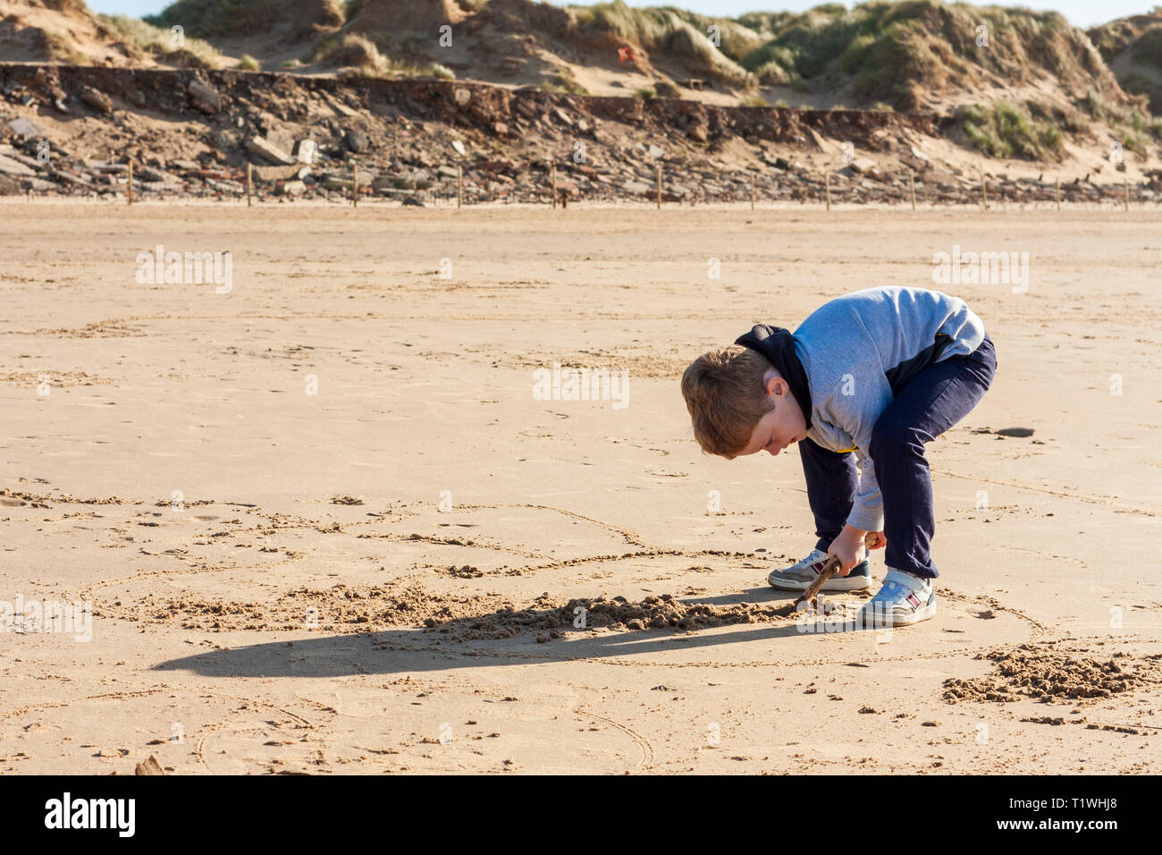 Un joven muchacho caucásico dibujar formas en la arena con un palo en Formby playa, Merseyside, Reino Unido. Foto de stock