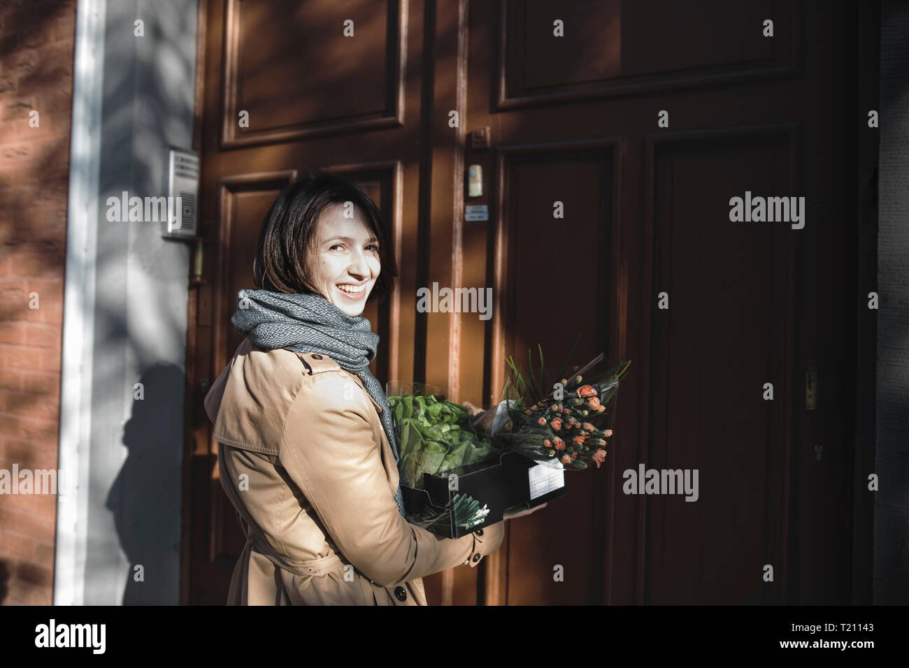 Retrato de mujer ríe con caja de cartón de compras de pie delante de la entrada de la casa Foto de stock