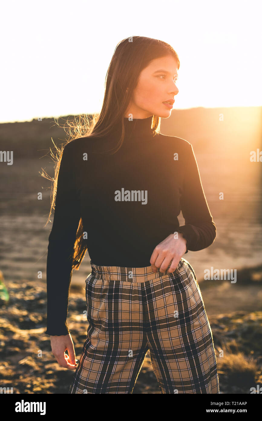 Retrato de moda adolescente vistiendo pantalón negro, suéter y comprobado al atardecer Foto de stock