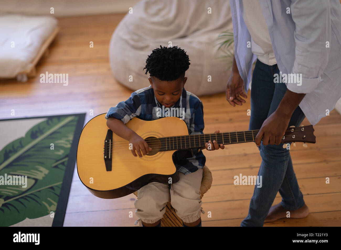 Padre ayudando a su hijo a tocar la guitarra en casa Foto de stock