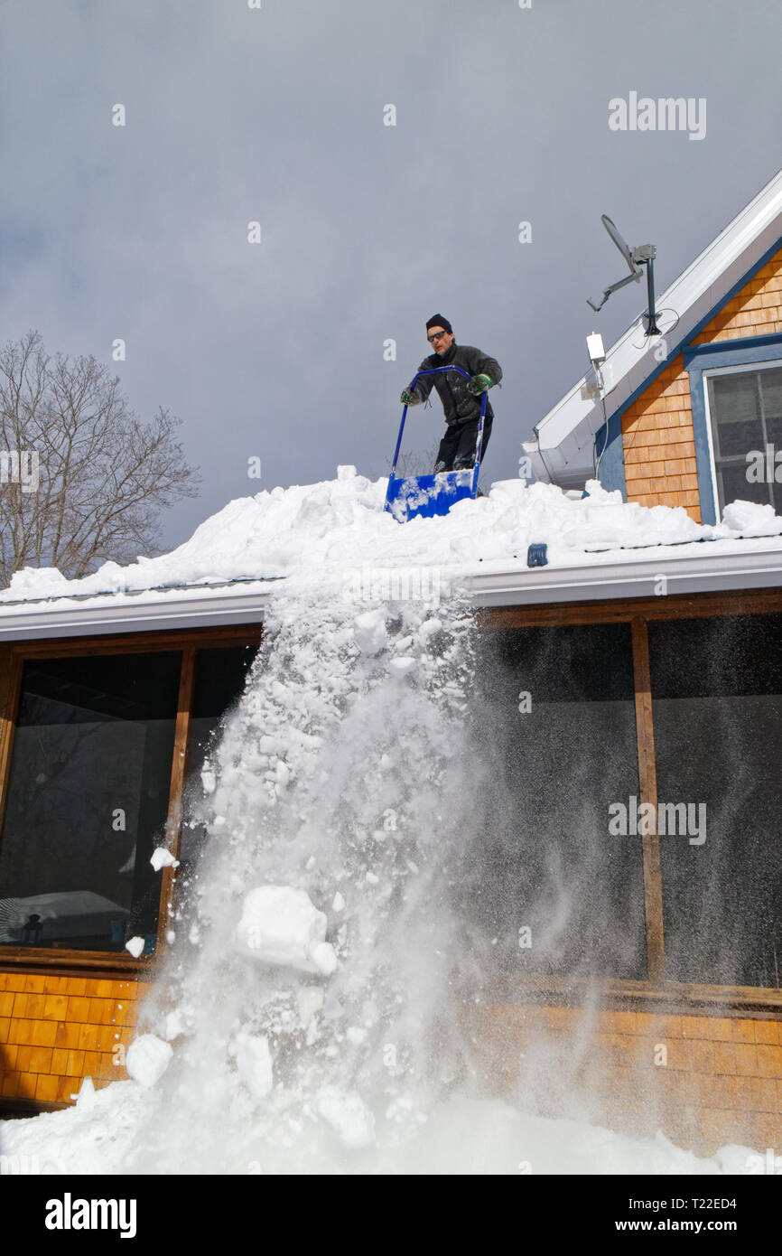 Un hombre en el tejado de su casa la retirada de nieve en Quebec. El invierno de 2018-2019 vio muy fuertes nevadas Foto de stock