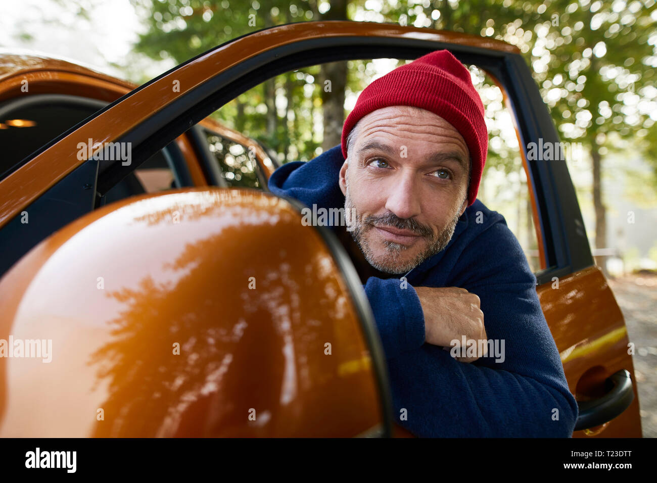 Retrato del hombre maduro barbado vistiendo gorra roja de asomarse a la ventana de Abrir puerta del automóvil Foto de stock