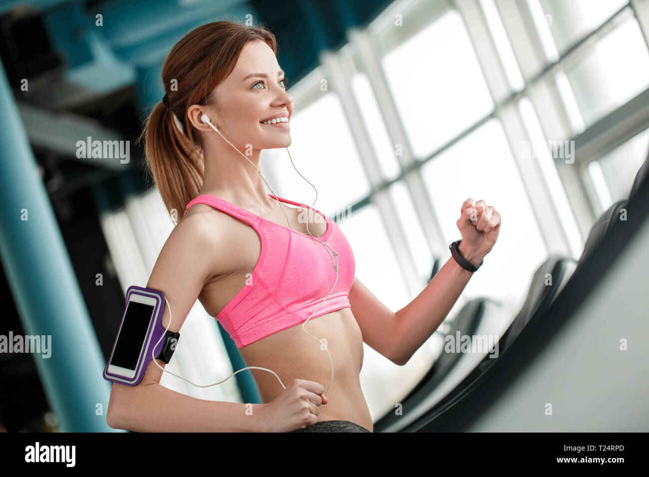 Ajuste a la mujer con auriculares y dispositivo móvil escuchando música en  la máquina de correr en el gimnasio Fotografía de stock - Alamy