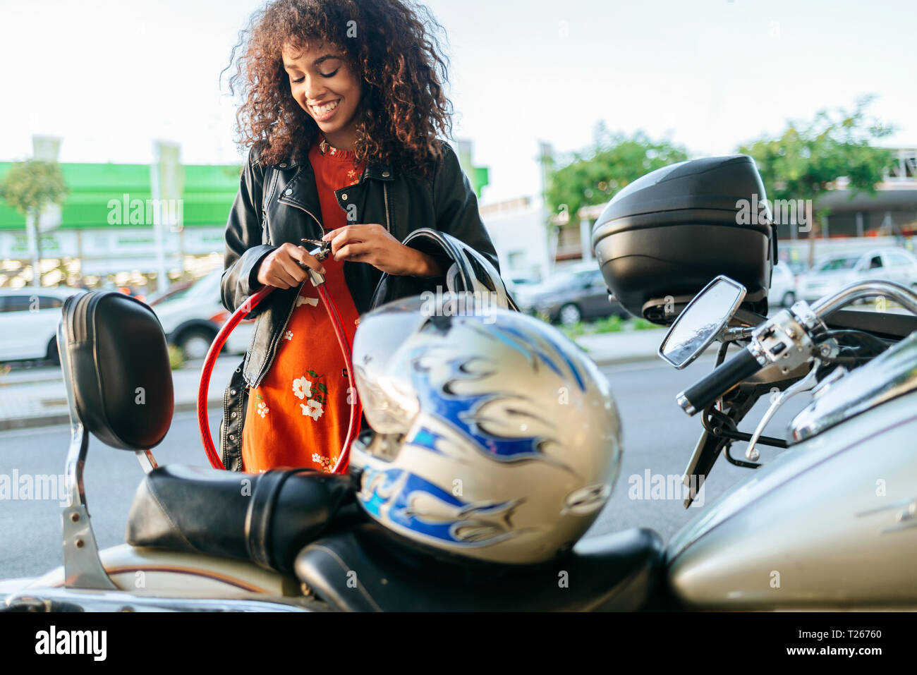 Mujer sonriente quitando el bloqueo de seguridad de su motocicleta Foto de stock