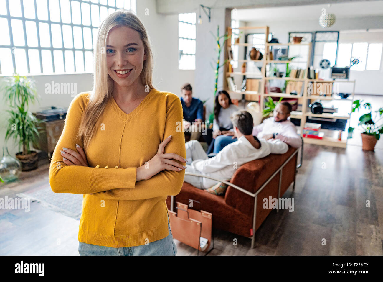 Retrato de sonriente joven empresaria con compañeros de trabajo en segundo plano en loft oficina Foto de stock
