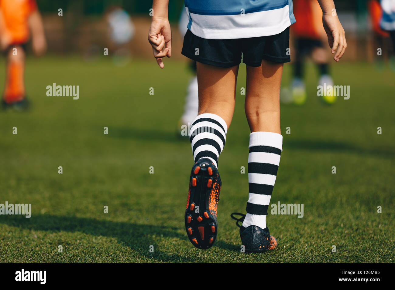 Las piernas del joven futbolista en botas de tacos de fútbol. Jugador  caminando sobre la hierba verde del campo de fútbol en el estadio. Close-up  de fútbol deportes de equipo Fotografía de