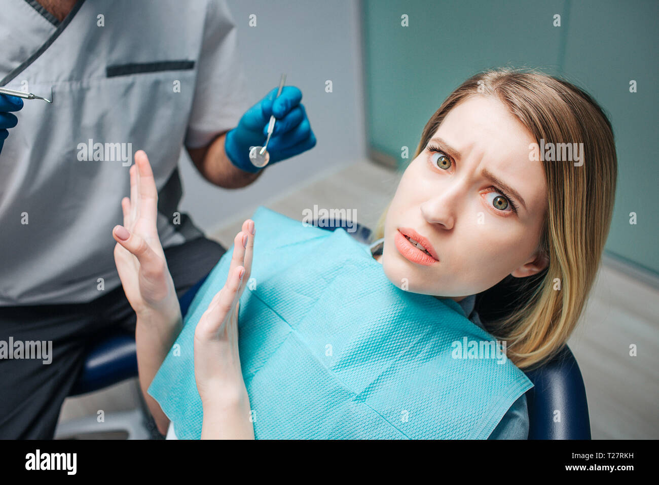Mujer joven mira asustado. Ella sentarse en la silla en odontología. La mujer mira a la cámara y empujar fuera médico. Él espera de herramienta del dentista. Foto de stock