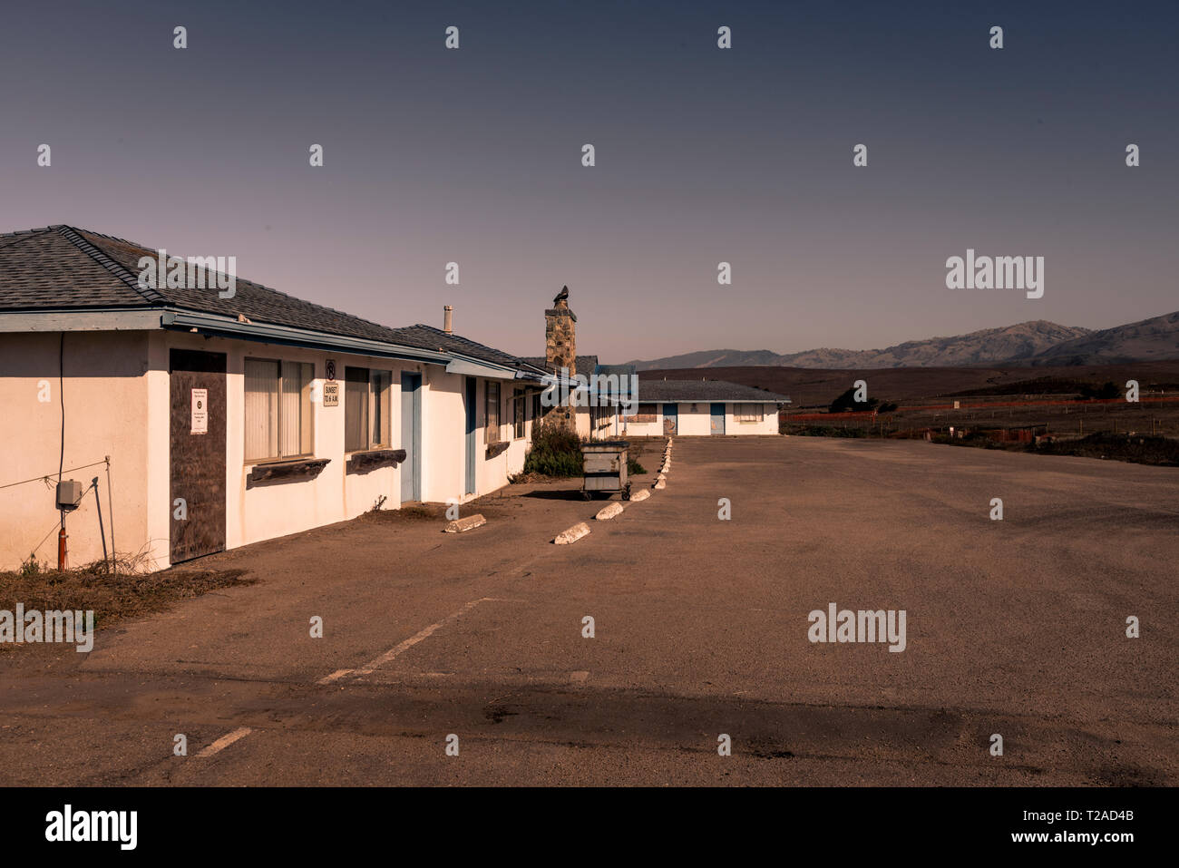 Viejo motel abandonados, el estacionamiento y las montañas más allá. Foto de stock