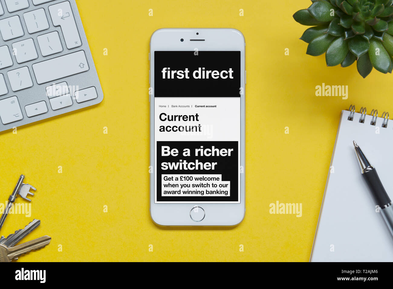 Un iPhone, mostrando el primer sitio web directo descansa sobre un fondo amarillo tabla con un teclado, teclas, bloc de notas y Planta (uso Editorial solamente). Foto de stock
