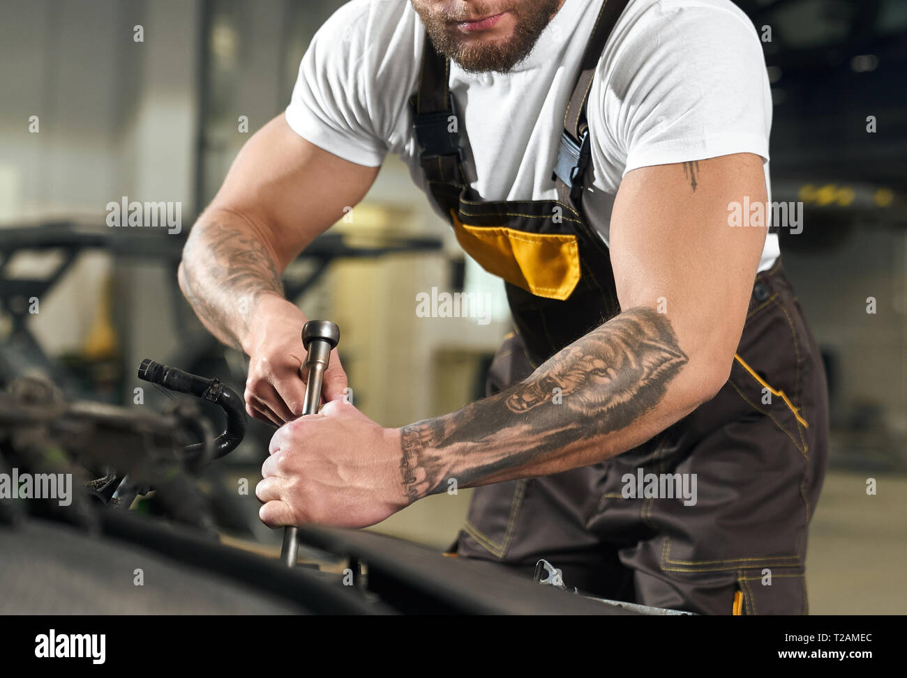 Vista lateral del macho fuerte musculatura mecánico con las manos y tatuaje  reparación de automóviles en auto servicio. Reparador de mono en la  fijación del motor en coche en w Fotografía de