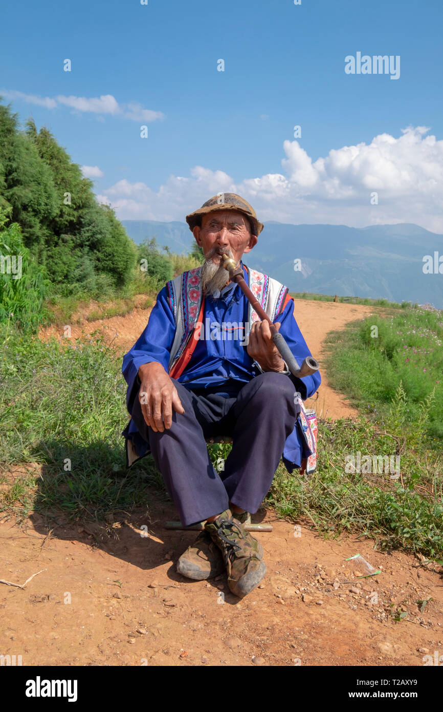 Hombre maduro local a fumar en pipa en una pequeña aldea en las montañas cerca de Kumming, en la provincia de Yunnan en el suroeste de China en septiembre Foto de stock