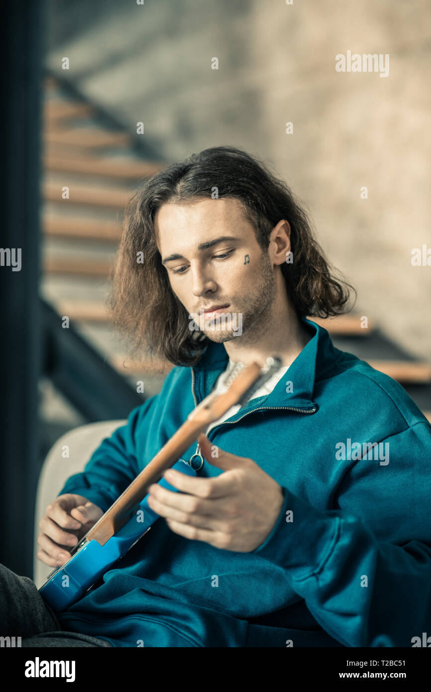 Descuidos guapo joven tonificación de cuerdas en su guitarra Foto de stock