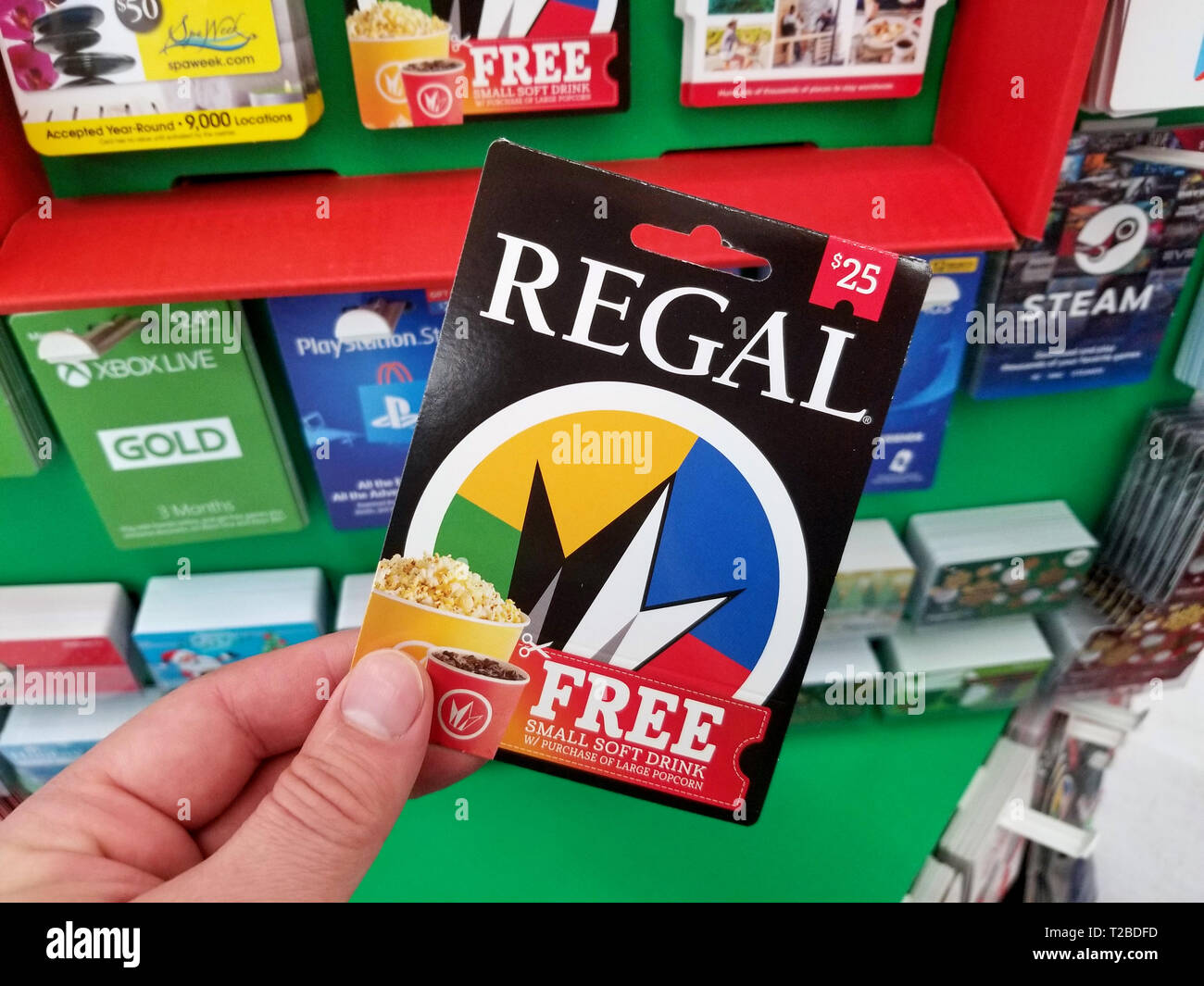 PLATTSBURGH, USA - Enero 21, 2019 : Regal Gift Card en una mano encima de  una estantería con diferentes tarjetas de regalos en una tienda de Walmart.  Regal es un llevándonos mult