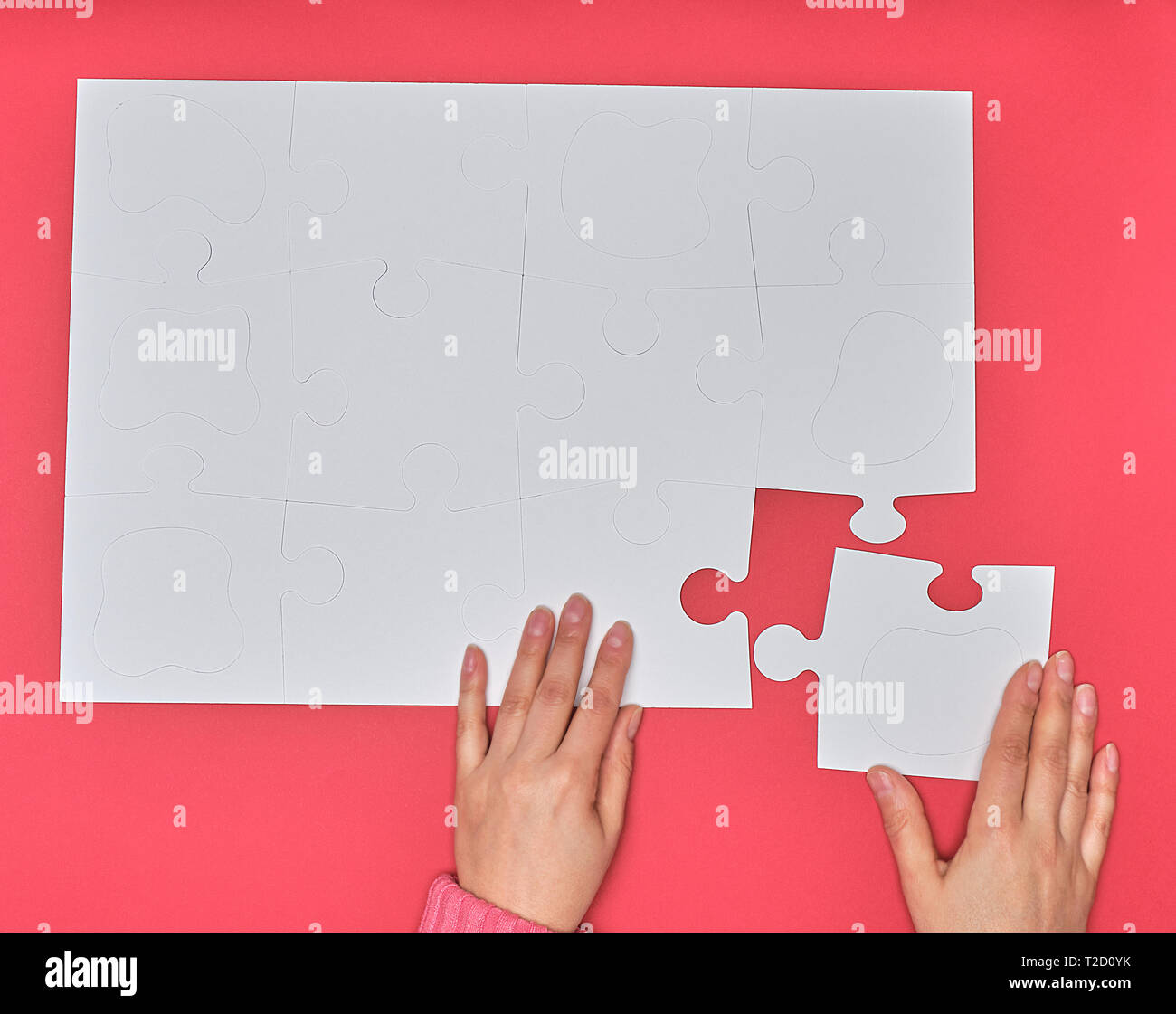 Mano femenina pone grande blanca puzzles en un fondo de color rosa, uno de los elementos que faltaban, vista superior Foto de stock