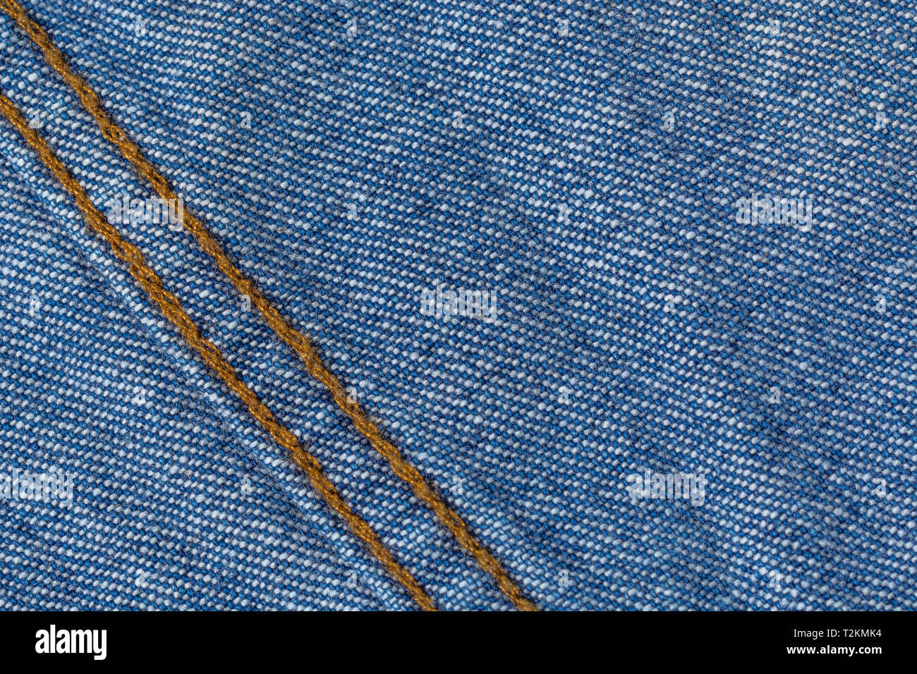 Primer plano de tela vaquera azul, mostrando patrón de trama de deformación y trama y costura naranja. Línea cosida, línea de puntos. Foto de stock