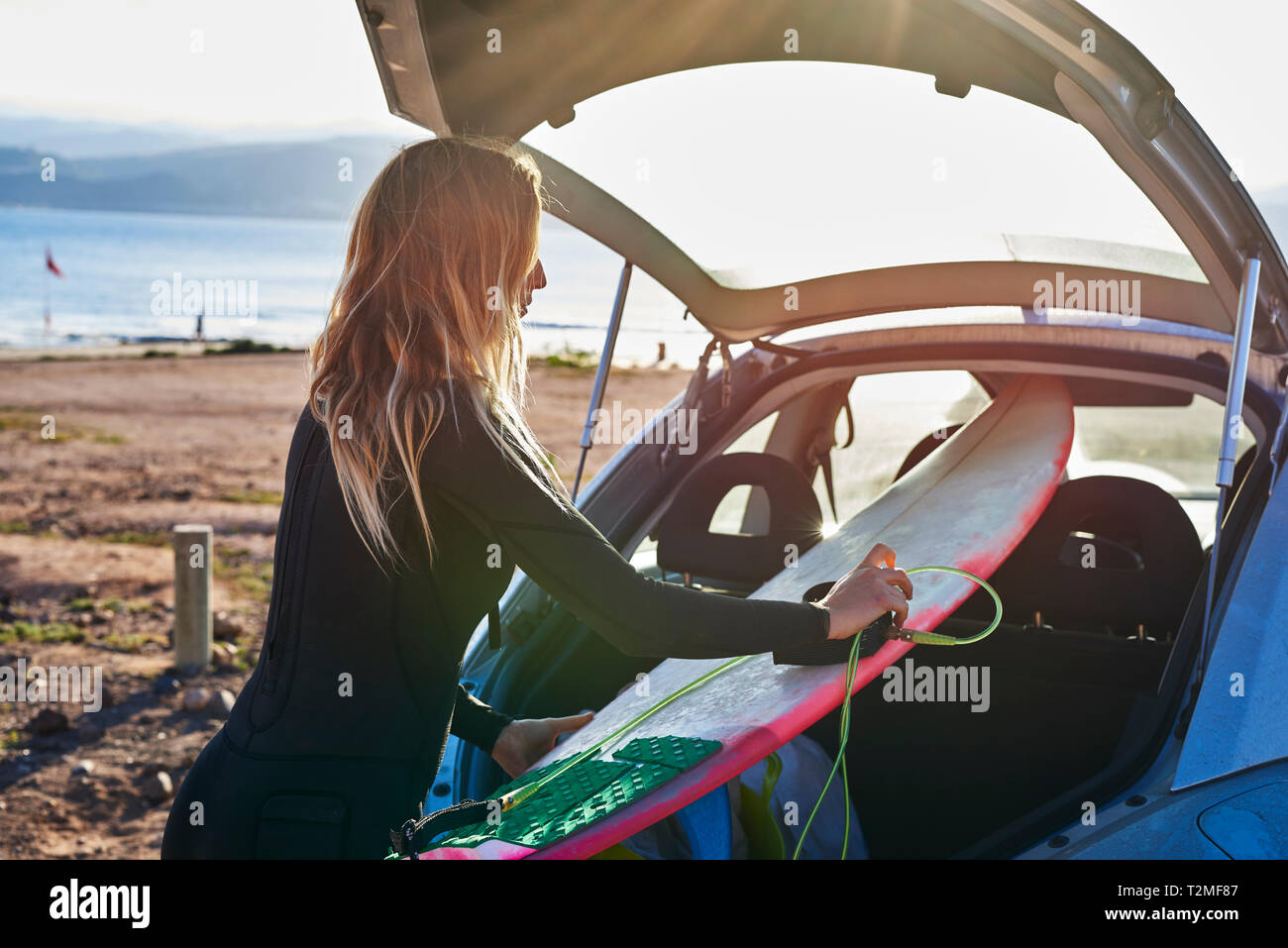 Mujer joven quitando tablas de surf desde el maletero del coche Foto de stock