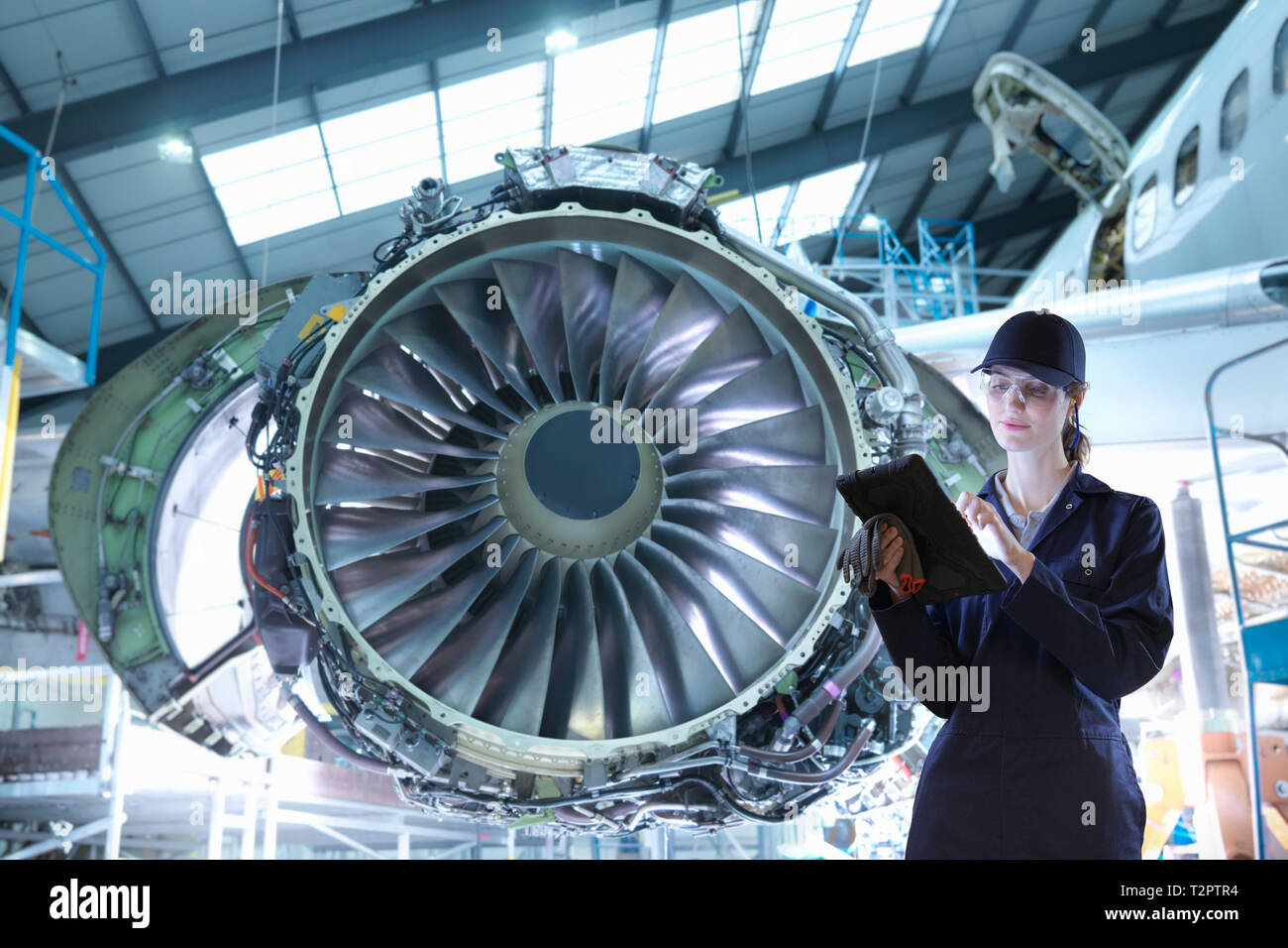 Imagen compuesta de trabajadora con tableta digital en fábrica de mantenimiento de aeronaves Foto de stock