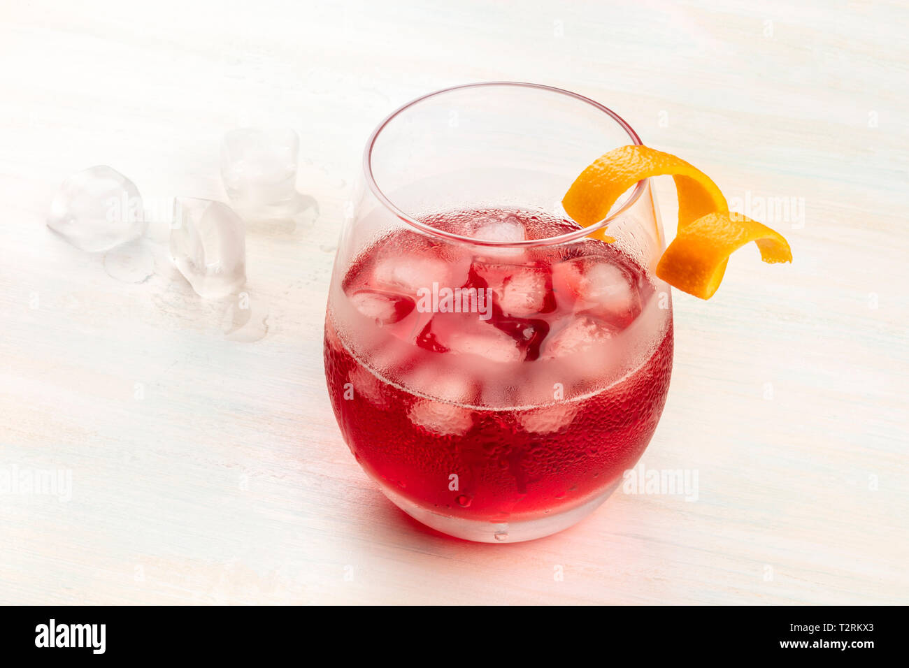 Una vibrante cóctel negroni con campari y una cáscara de naranja twist, con cubitos de hielo sobre un fondo de madera blanca, con espacio de copia Foto de stock