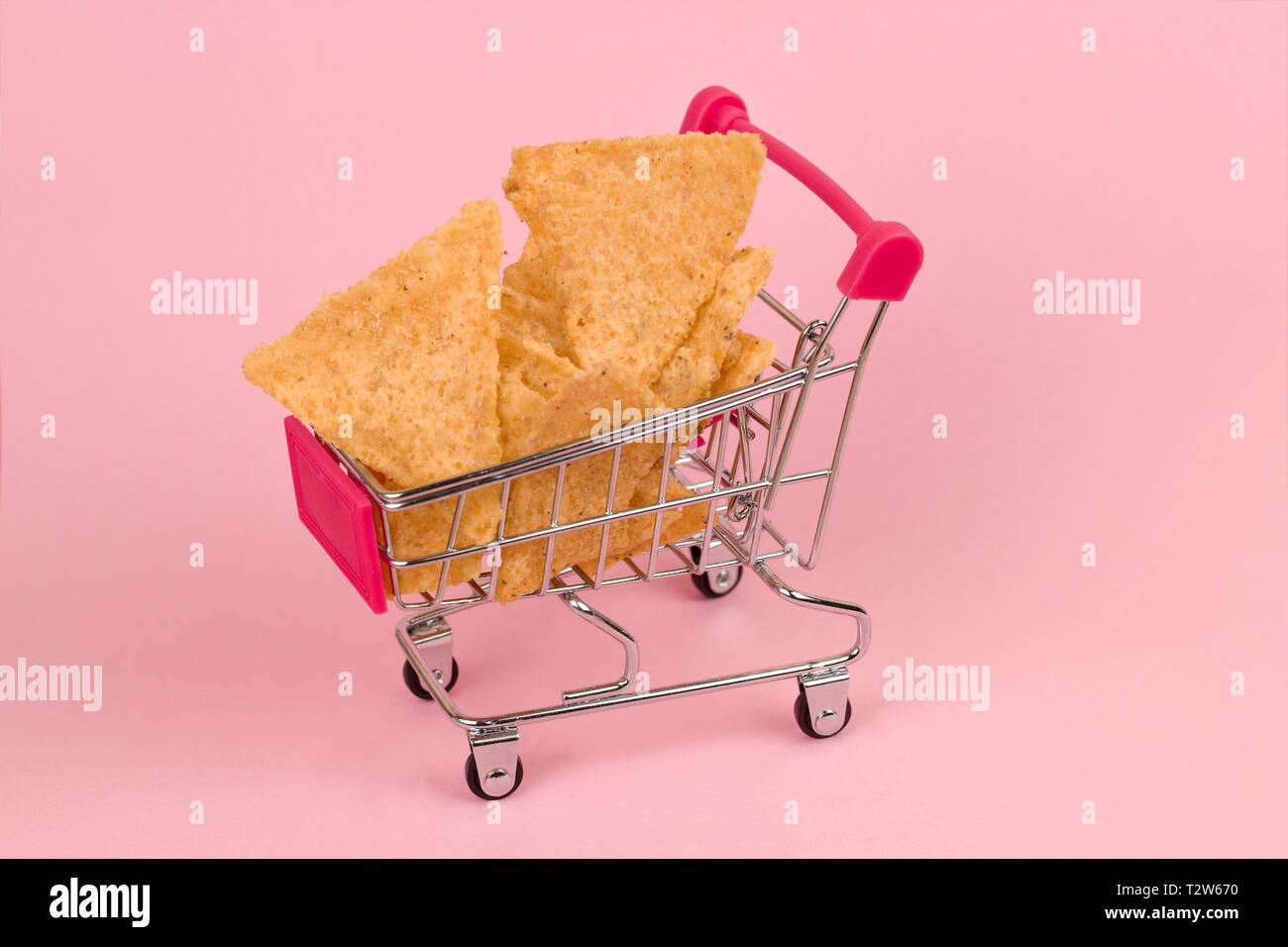 Compras lleno de nachos sobre fondo rosado pastel Foto de stock