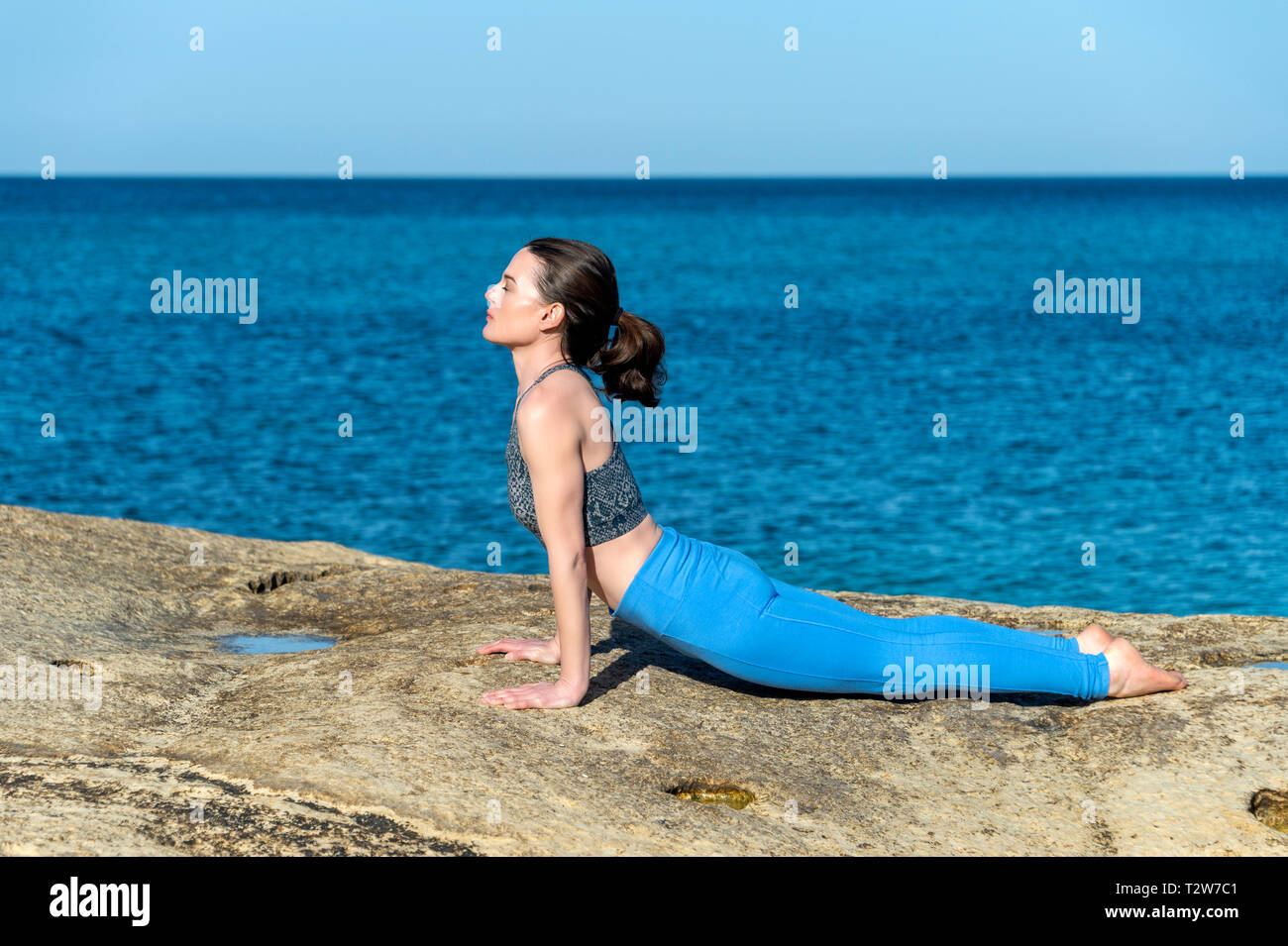 Mujer practicando yoga junto al mar, plantean el perro boca arriba. Foto de stock