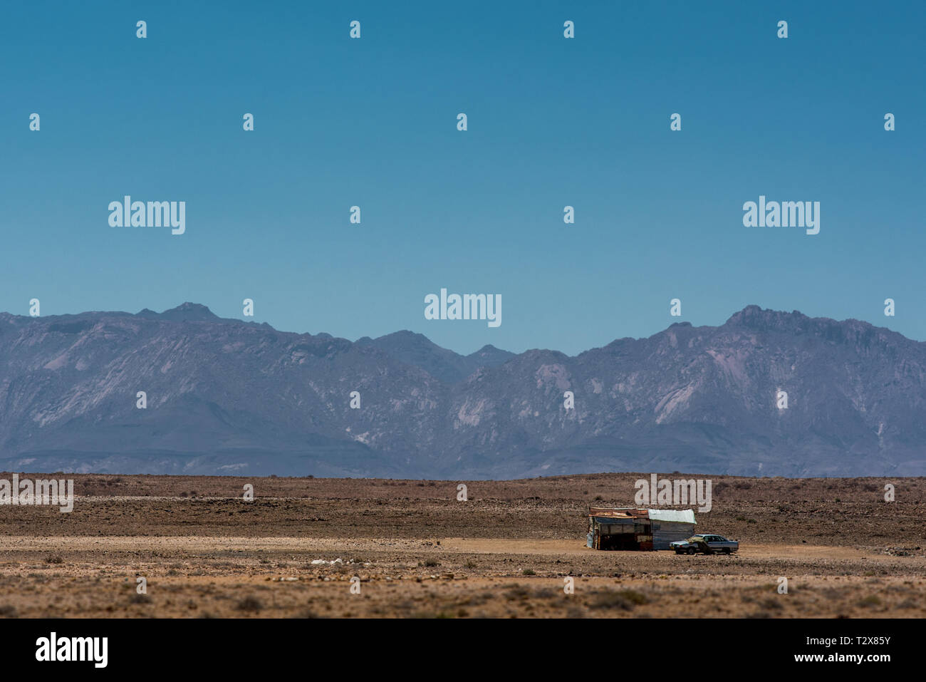 Una solitaria cabaña y coche en medio del vasto y seco paisaje de Namibia, con la montaña Brandberg en el fondo Foto de stock