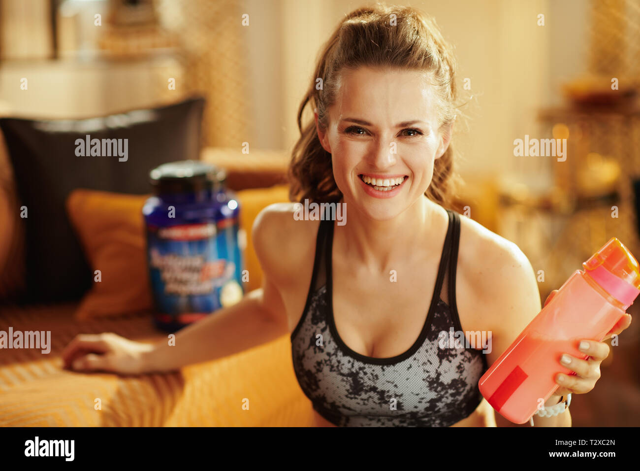 Feliz saludable Deportes mujer en ropa de gimnasia con agitador con suplementos de fitness en el hogar moderno. Foto de stock
