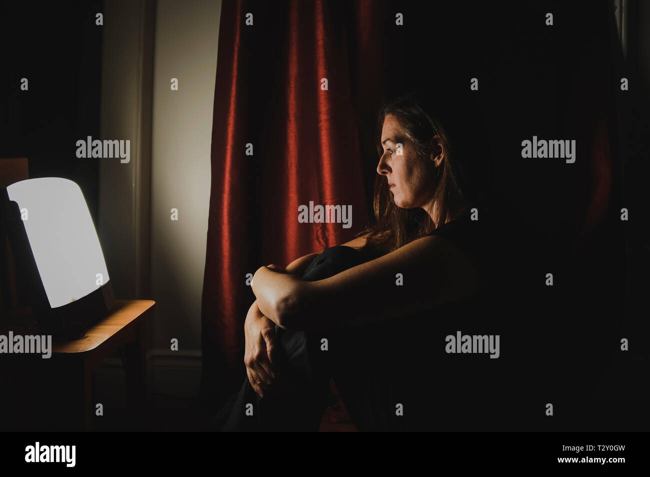 Perfil De Mujer Sentada Mirando A La Terapia De Luz Lámpara En Una Habitación Oscura Fotografía 2051