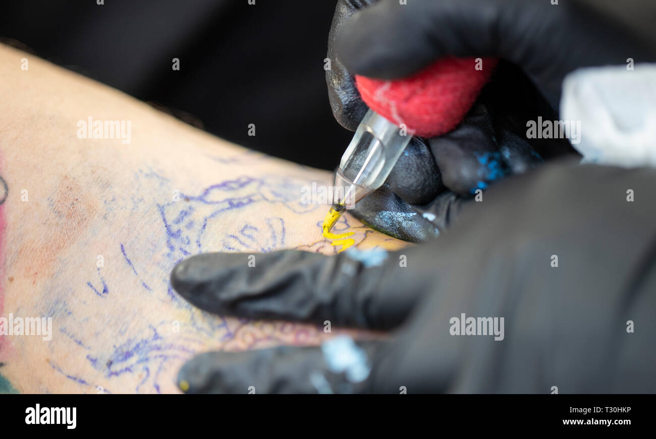 Primer plano de un tatuaje en la elaboración (aguja de tatuaje que aplica tinta  amarilla en la piel Fotografía de stock - Alamy