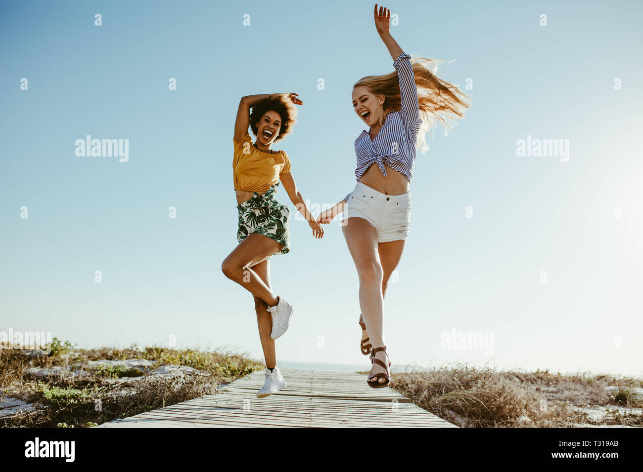 Dos amigas excitados corriendo con alegría en el paseo a lo largo de la playa. Dos mujeres disfrutando de vacaciones. Foto de stock
