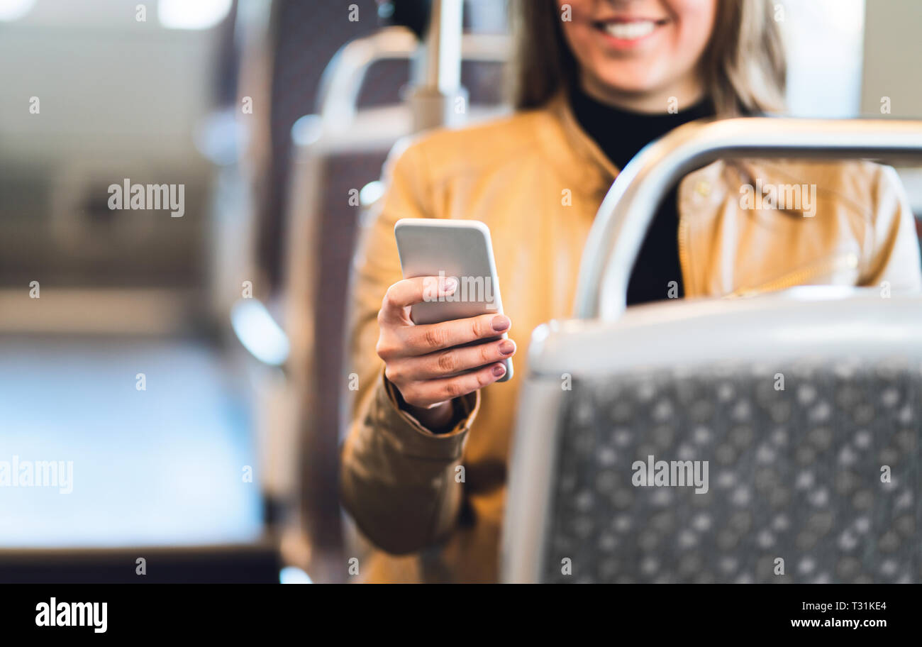 Mujer sonriente usando un teléfono inteligente en tren, metro, autobús o tranvía. Lady texting en transporte público o usando la conexión wi-fi gratuita. Foto de stock