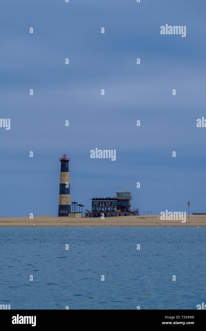 Rayas azules y blancas de Pelican Point Lighthouse junto al lodge encaramado sobre la franja de arena en el Océano Atlántico con birdlife en tierra Foto de stock