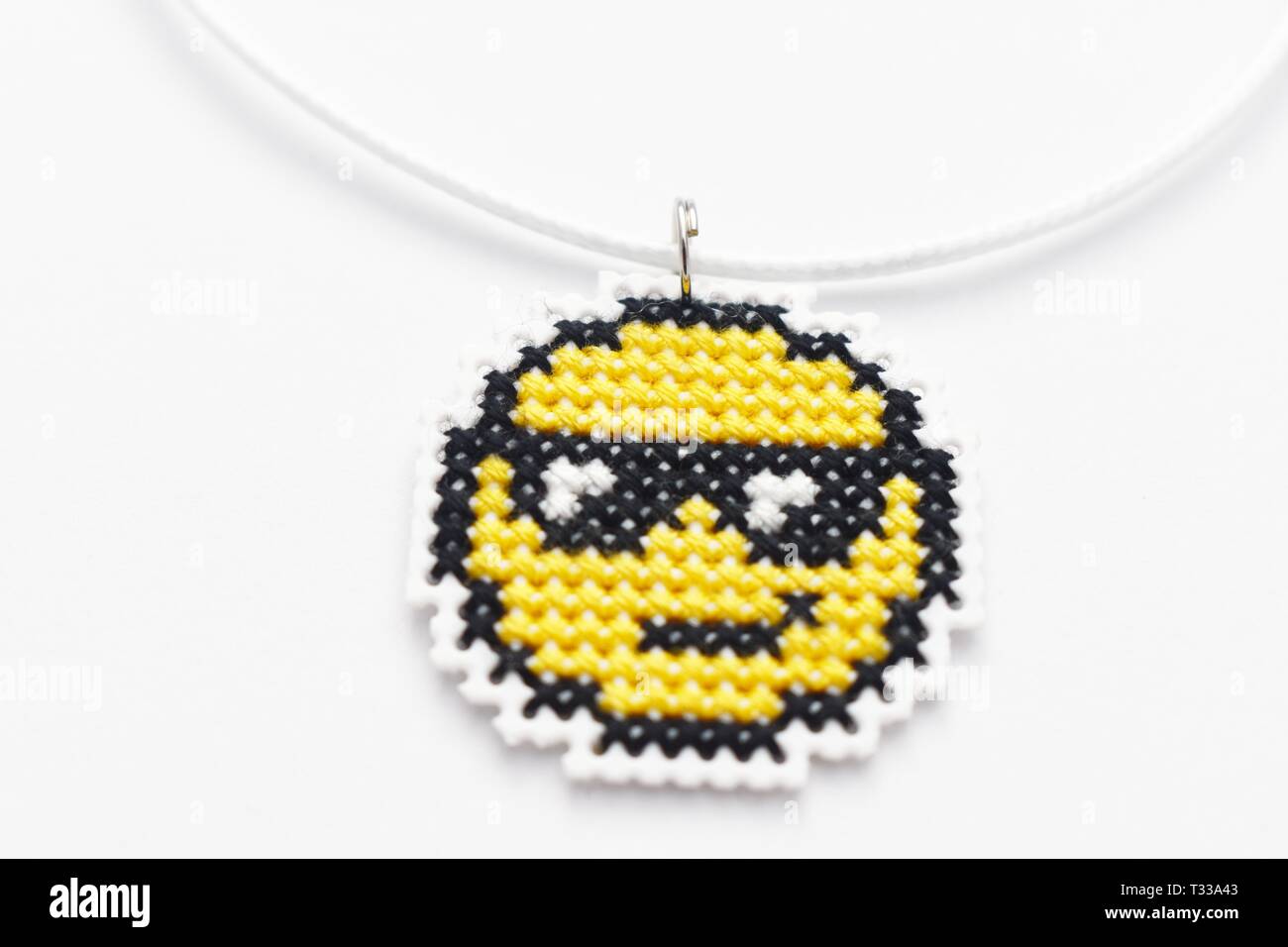 Punto de cruz Handmade necklace Emoji gafas de sol bordado sobre lienzo de plástico blanco. Foto de stock