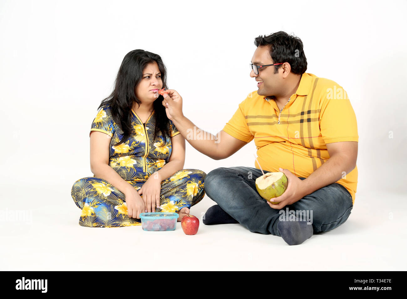 El hombre está comiendo sandía mujer embarazada con sentada en el suelo. Aislado en el fondo blanco. Foto de stock
