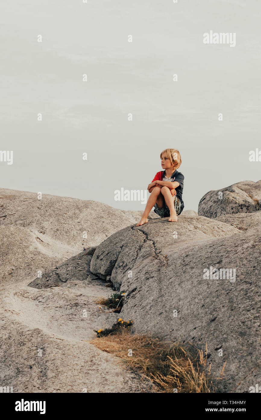 Muchacho sentado en las rocas, verdens ende Tjome, Tonsberg en Noruega Foto de stock