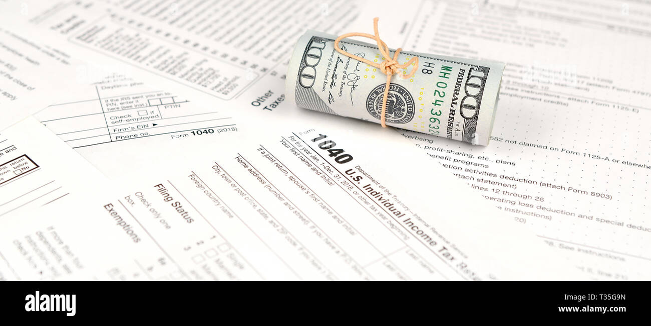 1040 Formulario de devolución de impuestos sobre la renta de las personas físicas con el rollo de billetes de dólar americano cerca. Concepto de período fiscal en Estados Unidos Foto de stock