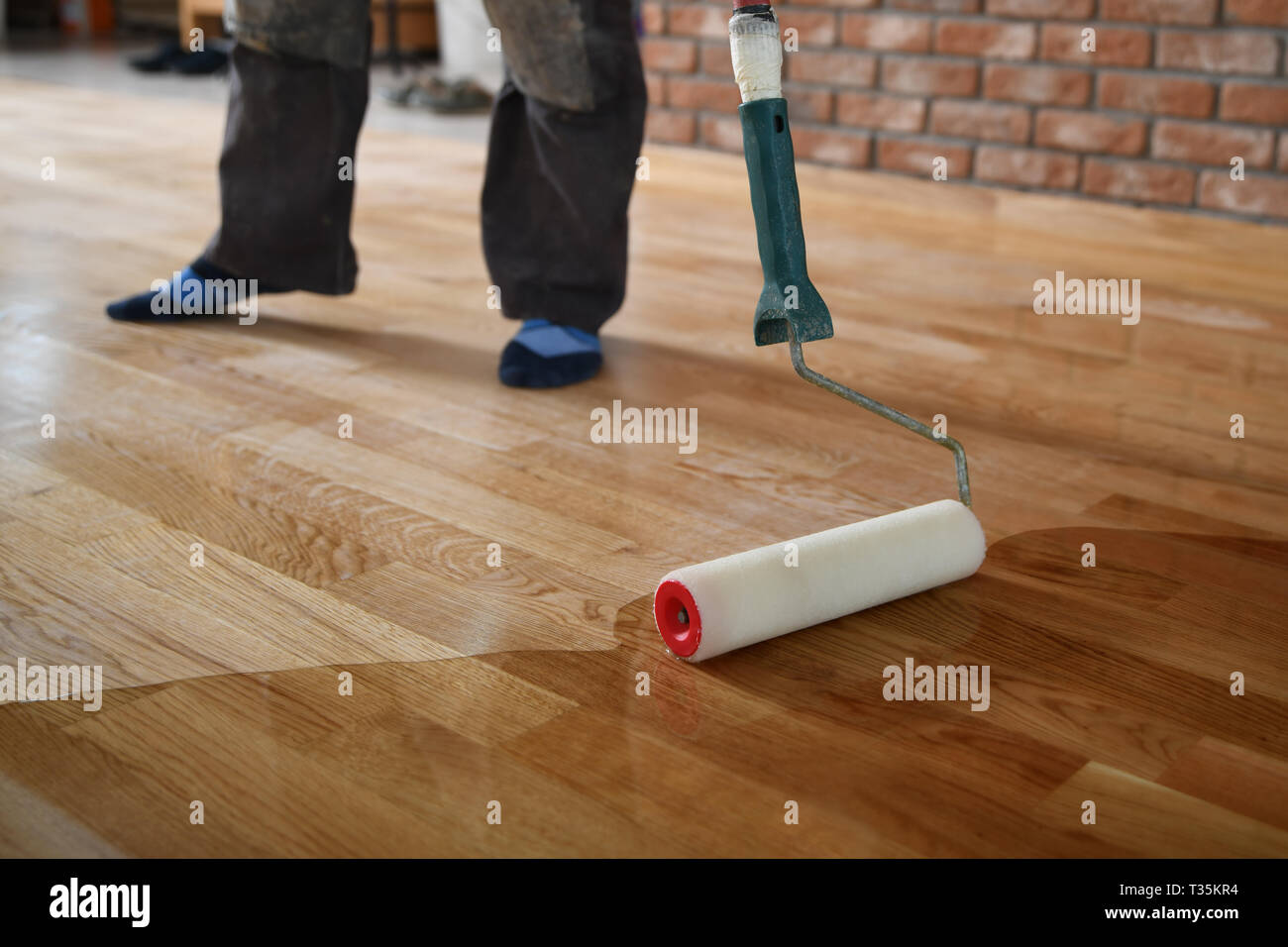 Lacado de pisos de madera. Trabajador usa un rodillo de revestimiento para  pisos. Barnizar parquet barnizado por rodillo de pintura - segunda capa.  Renovación de viviendas pa Fotografía de stock - Alamy