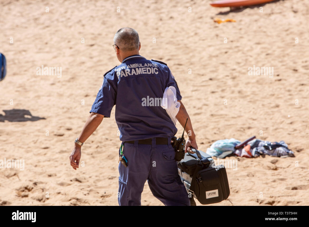Paramédico macho de NSW Ambulancia camina a través de la arena en Palm Beach para asistir un ahogamiento inminente víctima quien fue salvado por los voluntarios de rescate de surf,Sydney, Foto de stock