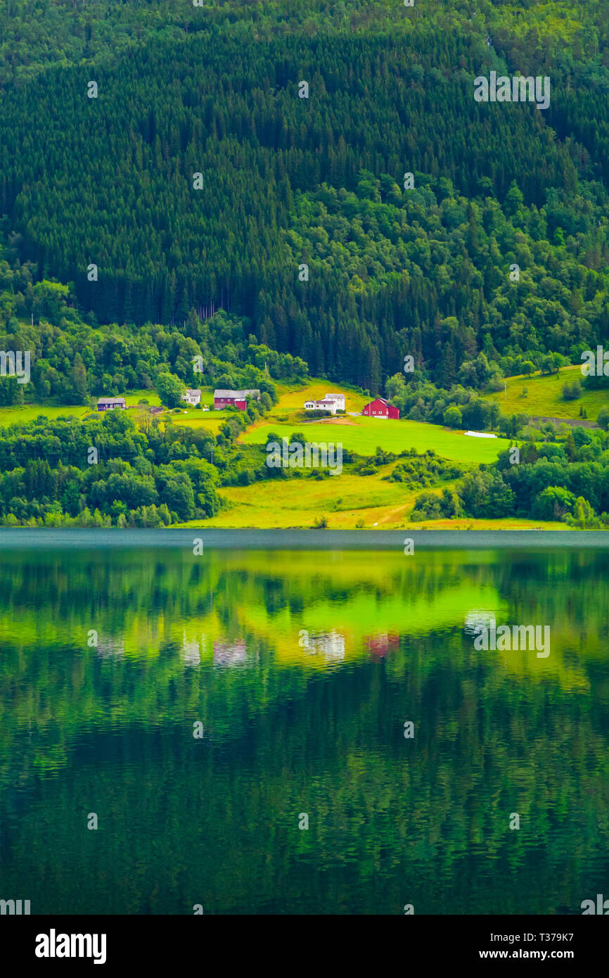 Colorido pueblo a orillas del lago alpino, a los pies de la montaña boscosa pendiente. Una pequeña aldea con casas modernas por el lago, Noruega. Las ventanas Foto de stock