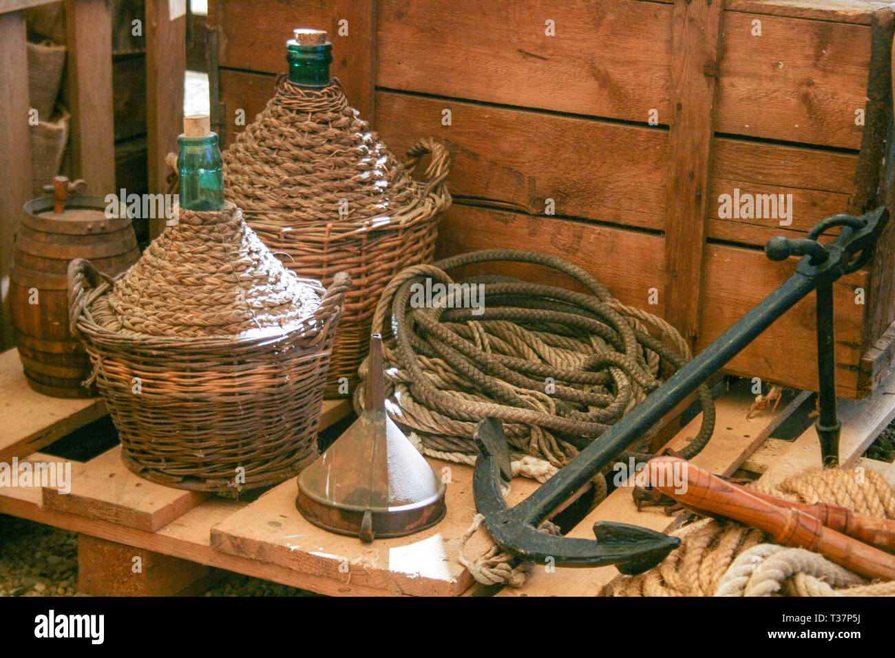 Composición con carro de madera vieja y vino viejo matraces con cuerda y ancla en Italia Foto de stock