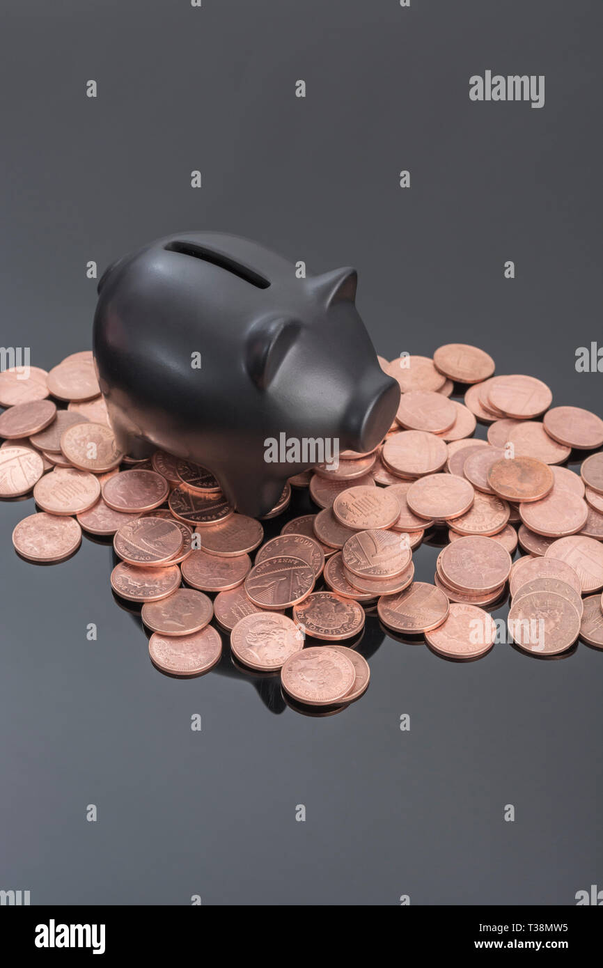 Hucha de cerámica negra con monedas británicas sobre fondo negro reflectante. Metáfora para ahorrar dinero, los ahorros personales, Ahorrar centavos, British pennies. Foto de stock