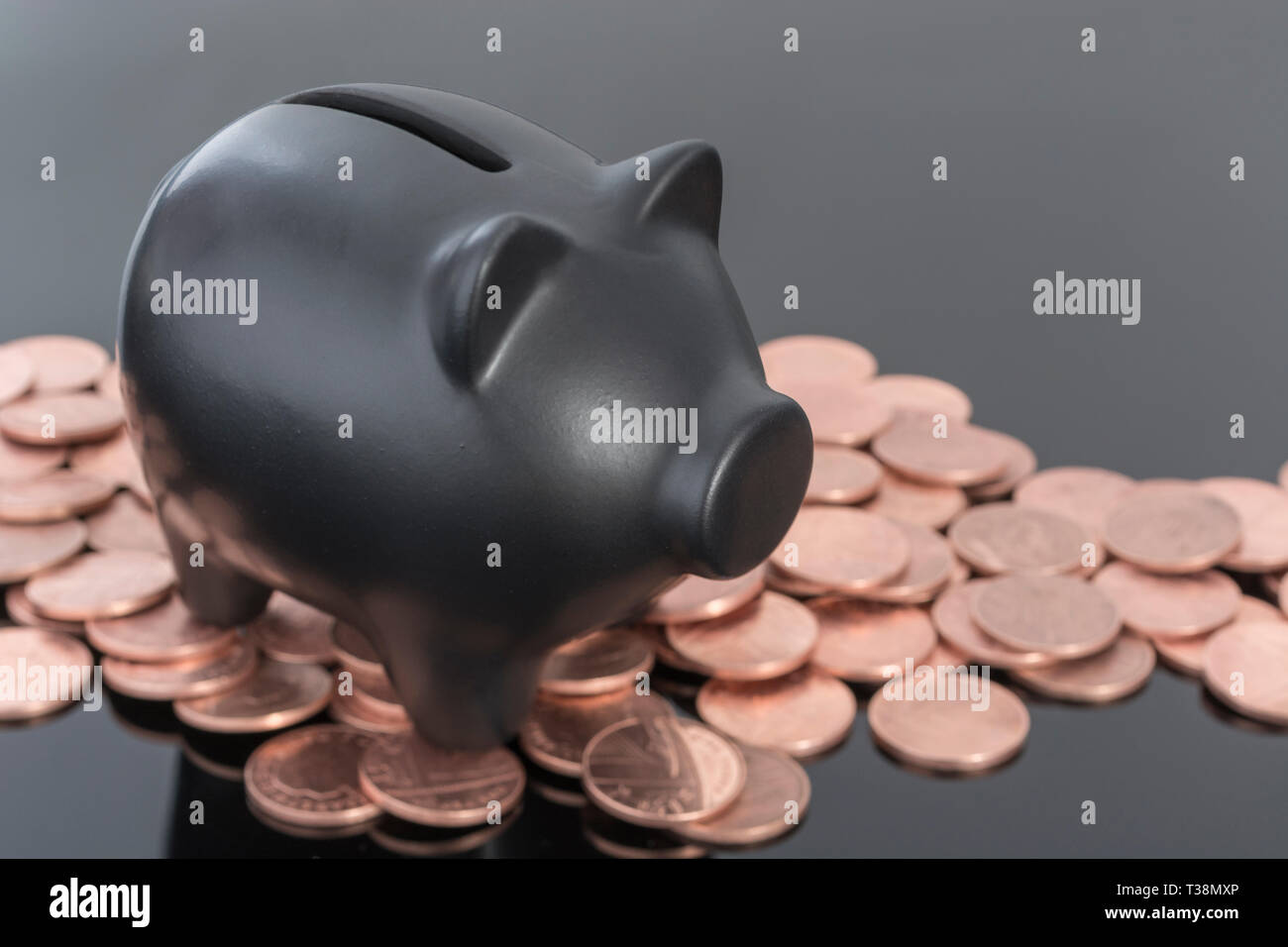 Hucha de cerámica negra con monedas británicas sobre fondo negro reflectante. Metáfora para ahorrar dinero, los ahorros personales, Ahorrar centavos, British pennies. Foto de stock