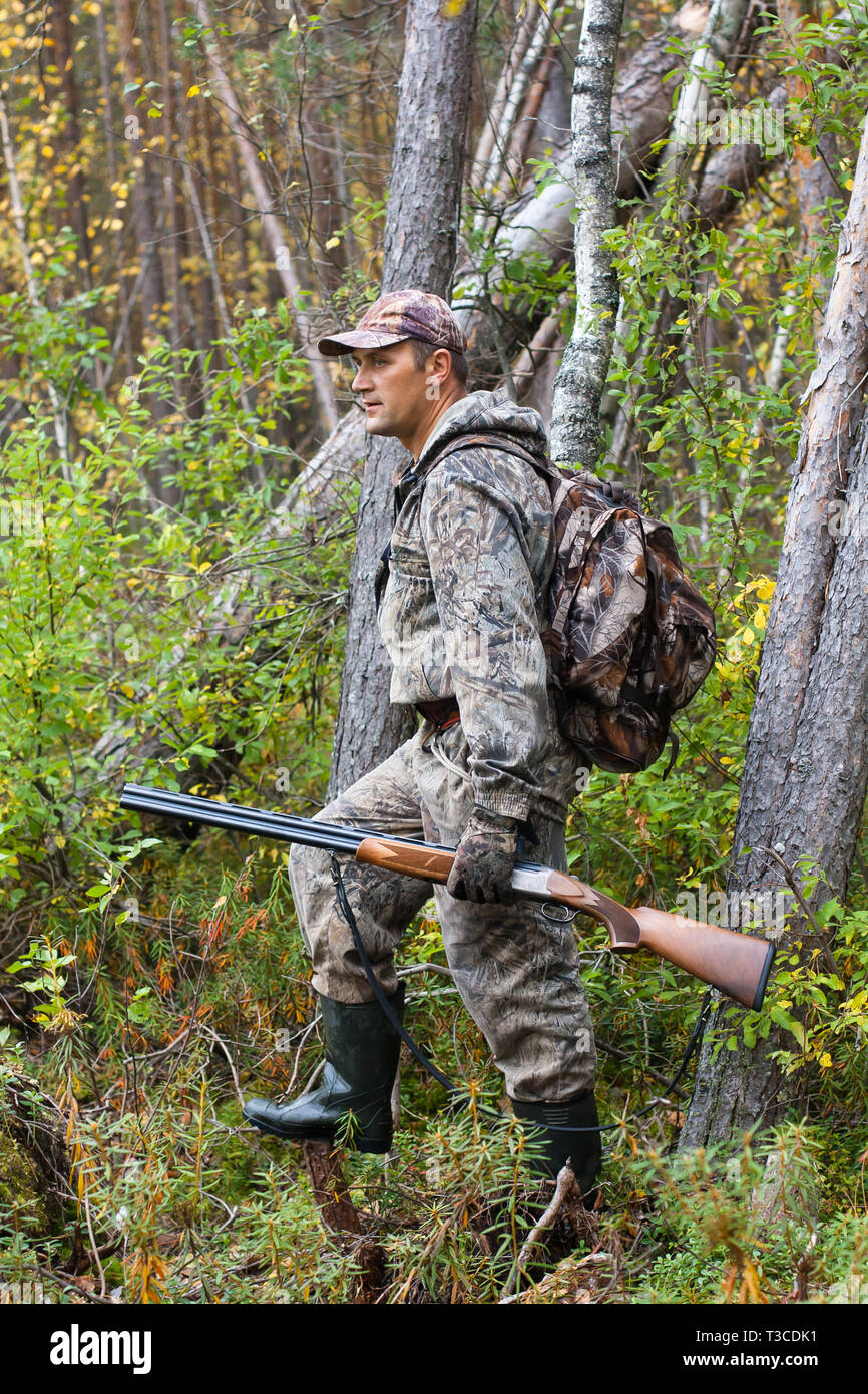 En camuflaje de cazador con escopeta de caza y la mochila en el bosque de  pinos Fotografía de stock - Alamy