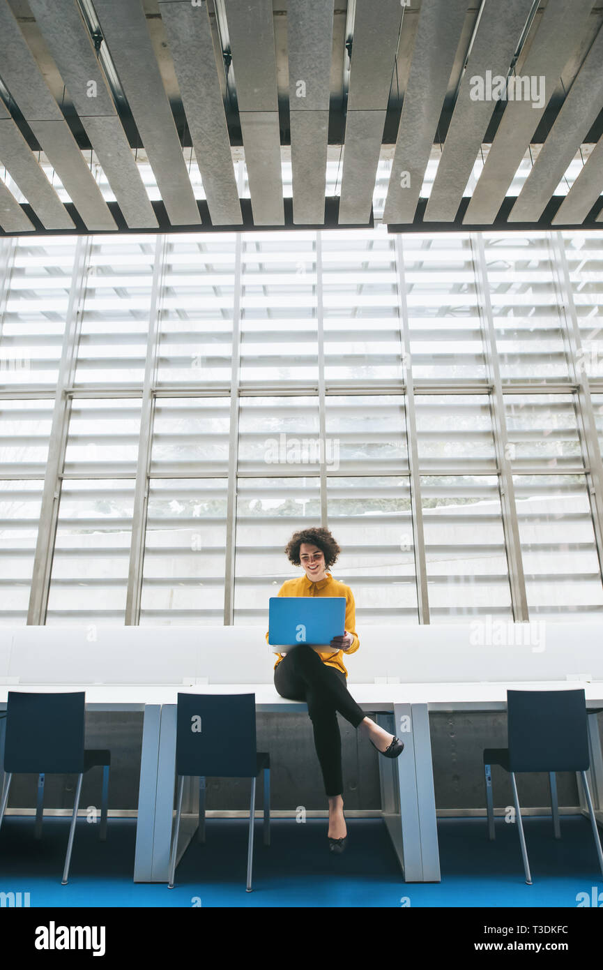 Joven estudiante o empresaria sentada en su escritorio en la habitación en una biblioteca u oficina, utilizando el portátil. Foto de stock