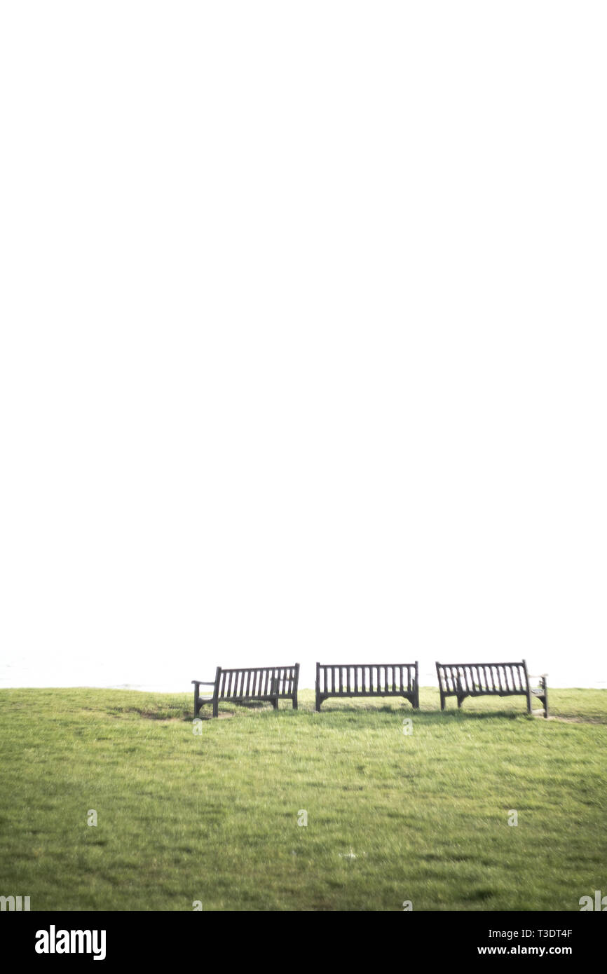 Tres bancos en la hierba con el espacio en blanco que habrá por encima (Copiar área vacía), podría simbolizar la soledad, el vacío, la depresión, la tranquilidad, la evasión. Foto de stock