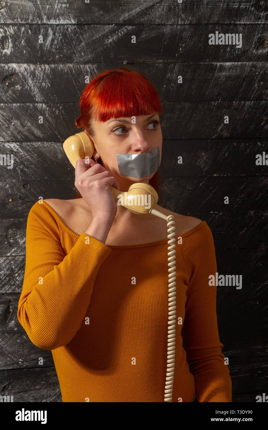 Imagen conceptual. Joven chica pelirroja intenta hablar por teléfono con selladas con cinta adhesiva con sus labios para que ella mantiene silencio Foto de stock