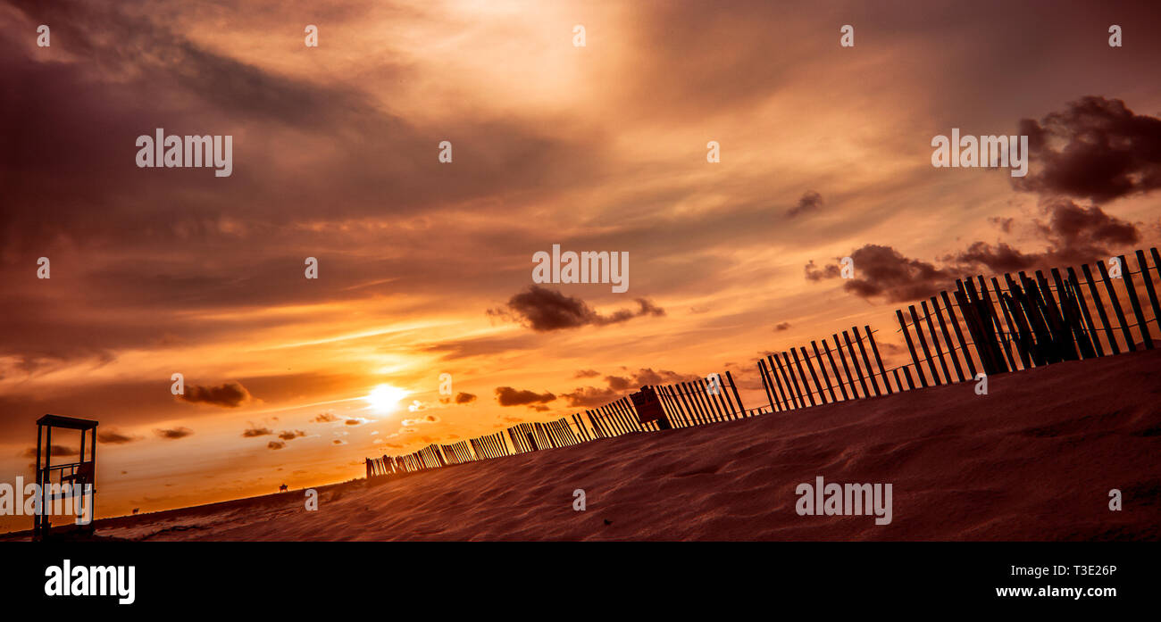 El sol se pone detrás de una valla de listones de madera y arena en el extremo oeste de Dauphin Island, Alabama. Cercas de arena se utilizan para el control de la erosión. Foto de stock