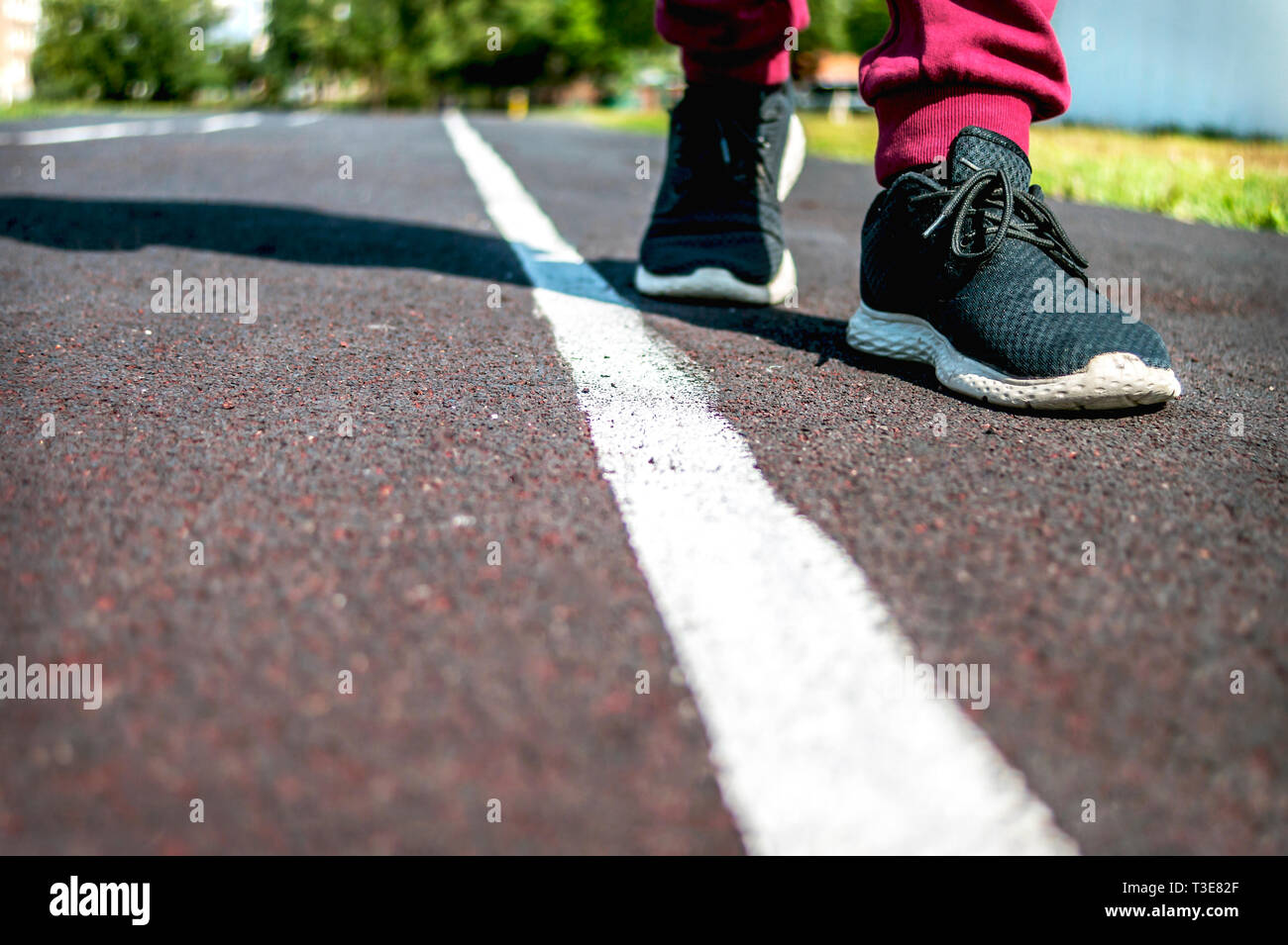 Un niño en zapatillas paseos a lo largo de la línea blanca en la pista de  atletismo en un día de verano. Hacer la elección, al cruzar la frontera.  Concepto de restricción.