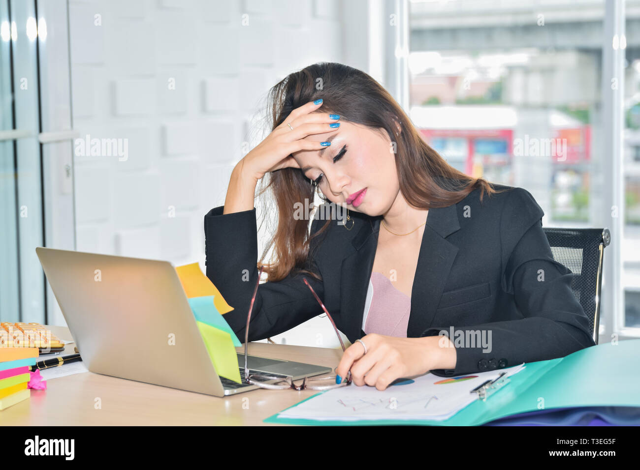 Subrayó mujer de negocios sentada y sosteniendo la cabeza a causa de dolor cefalea en oficina moderna Foto de stock