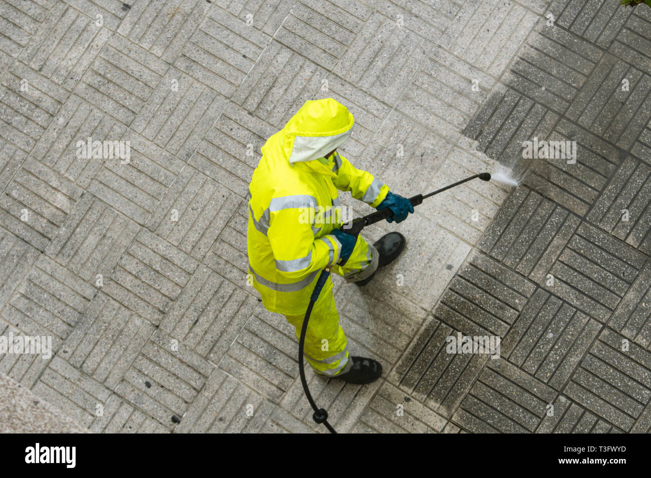 Vista superior de un trabajador de la limpieza de la acera de la calle con el chorro de agua de alta presión. Concepto de mantenimiento público Foto de stock