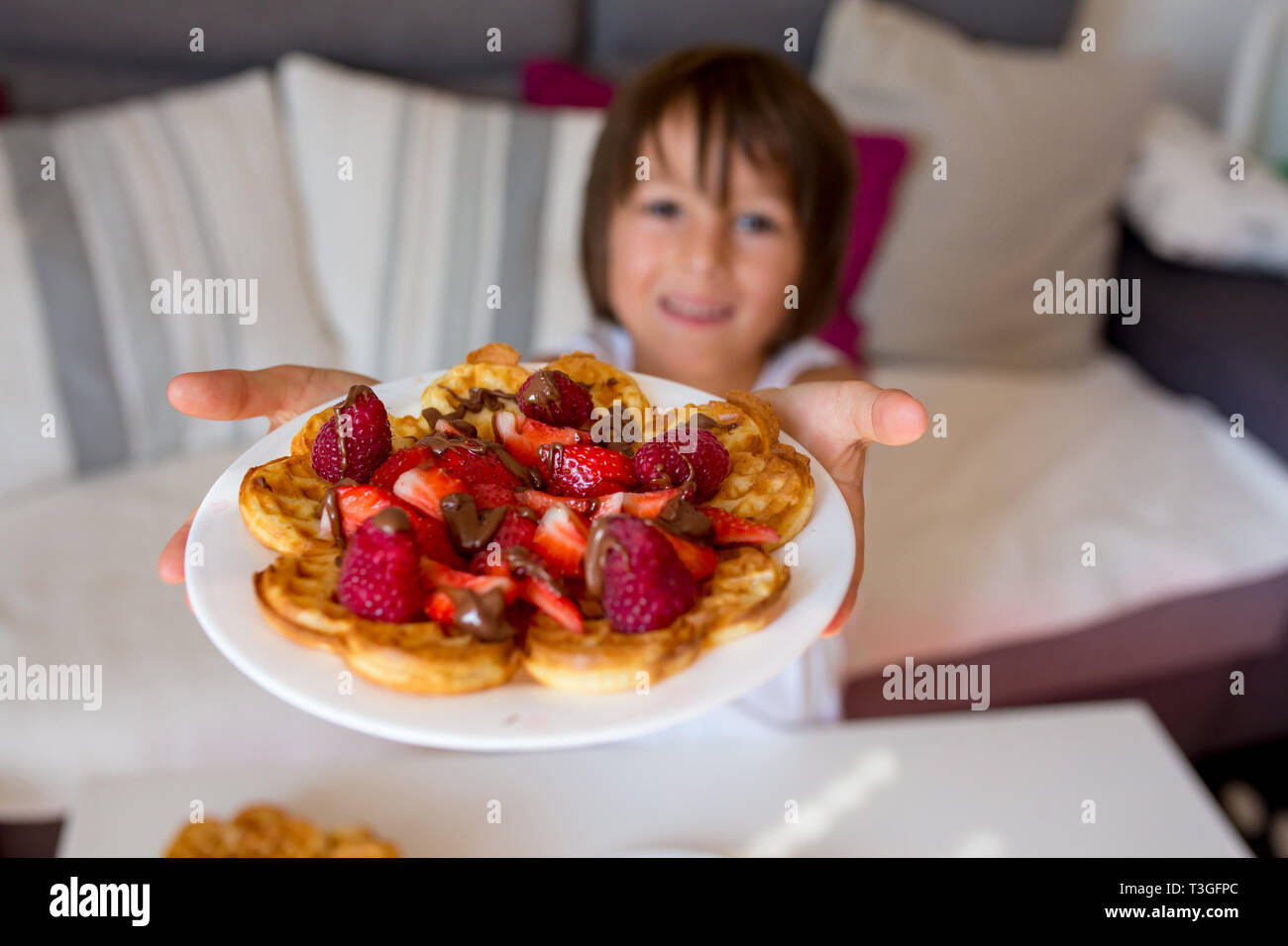 Dulce niño cumpleaños comiendo gofre belga con fresas, frambuesas y chocolate en casa Foto de stock
